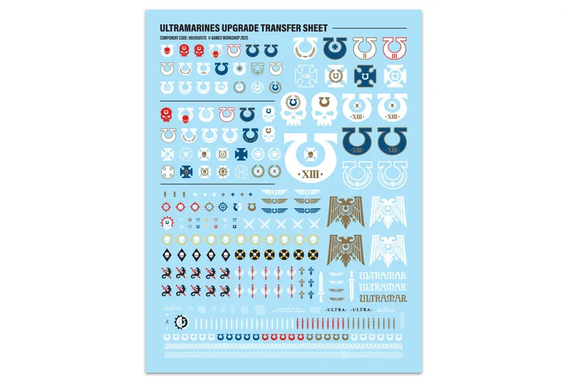 A transfer sheet featuring a variety of Ultramarines decals, set against a light blue background. The sheet includes campaign badges, veterancy markings, and multiple variants of the Ultramarines Chapter icon, along with symbols like skulls, wings, and laurels. Decorative borders and trim decals are also present, providing options for customizing models with additional flair.