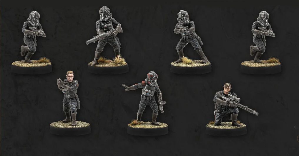 Seven miniatures are displayed against a dark background, showcasing the Imperial Special Forces from Star Wars: Legion. The figures include various troopers in tactical gear, some holding blasters and others in dynamic poses, with details like helmets and insignia visible. The bases are textured with grass, adding to the realistic appearance of the miniatures.