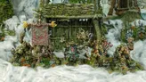 A group of intricately detailed miniatures inspired by Celtic mythology is displayed in front of a rustic, weathered structure covered in moss and foliage. The miniatures, depicting various fantastical creatures, include a central figure holding a banner, flanked by others wielding weapons and adorned with unique features like tusks and intricate patterns. The scene is set amidst a misty, ethereal atmosphere, enhancing the mystical theme of the Famhairean campaign.