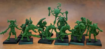 A collection of old school miniatures from Satyr Art Studio, featuring various fantastical creatures in a vibrant green color. The figures include beastmen with distinct features such as horns and claws, some wielding weapons, and a central figure holding a staff topped with a skull and a crescent. They are displayed on black bases against a warm, textured background.