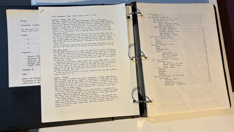 A three-ring binder contains a playtest manuscript for "ManaStorm: The Magic Adventure Game," featuring several loose character sheets and a core mechanics cheat sheet. The cheat sheet outlines key concepts such as Aspects, Vitality, and Life, detailing how each character has five Aspects linked to the Colors of Magic, along with a Hero Deck that represents their control over mana. The visible pages include character concepts, goals, and mechanics for gameplay, emphasizing the game's connection to the Magic: The Gathering universe.