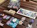 Board game Nakasendo box with illustrated cover, open on wooden surface. Components include wooden tiles, small cardboard pieces with snowflakes and buildings, and a cloth map bag with decorative patches. Game cards display scenes of snowy landscapes and structures.
