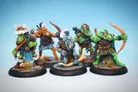 Five colorful orc miniatures are displayed against a light blue background. Each figure is uniquely designed, showcasing various poses and weapons: one orc wields a bow, another holds a club, while a third has a spear. They are adorned in armor with intricate details, including fur accents and decorative elements, standing on textured bases with tufts of grass. The overall scene highlights the vibrant colors and craftsmanship of the miniatures.