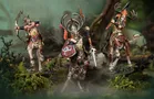 A trio of elven centaur models from the Kurnoth’s Heralds warband stands prominently in a lush, forested setting. Each figure is intricately detailed, featuring ornate armor and antlered helmets, with vibrant colors highlighting their unique designs. The central figure wields a spear and shield, while the others are posed with weapons, showcasing their readiness for battle amidst a backdrop of moss and twisted branches.