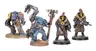 Three miniatures from the Palanite Enforcer Captains & Sergeants set are displayed. On the left, a figure wields a large axe and wears a blue and brown uniform with a fur collar, while the two figures on the right are equipped with firearms and feature distinctive yellow masks and red mohawks. All three are mounted on circular bases, showcasing intricate details in their armor and accessories.