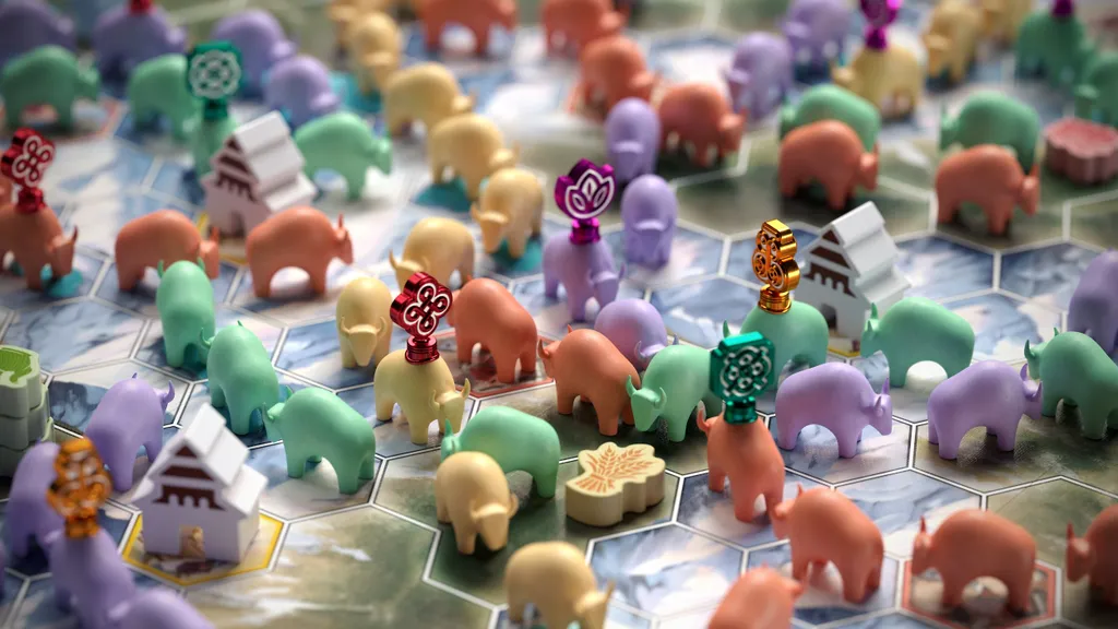 Colorful plastic yak miniatures in various poses on a hexagonal board with light blue and white terrain. Some yaks wear decorative headpieces in gold, purple, and red. Small brown and green tokens with floral designs are scattered among them.